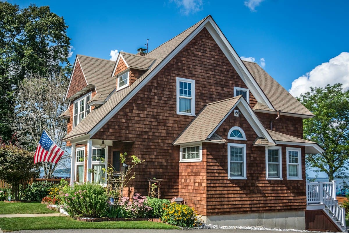 A brown shingle-style American home with a flag