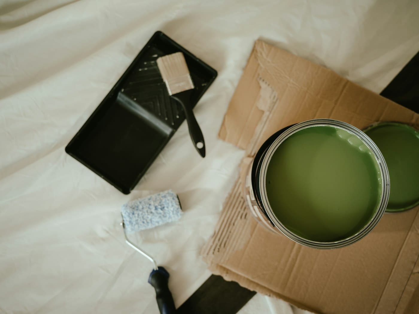 Overhead flat-lay of a paint tray, brush, roller and open paint can on a drop cloth
