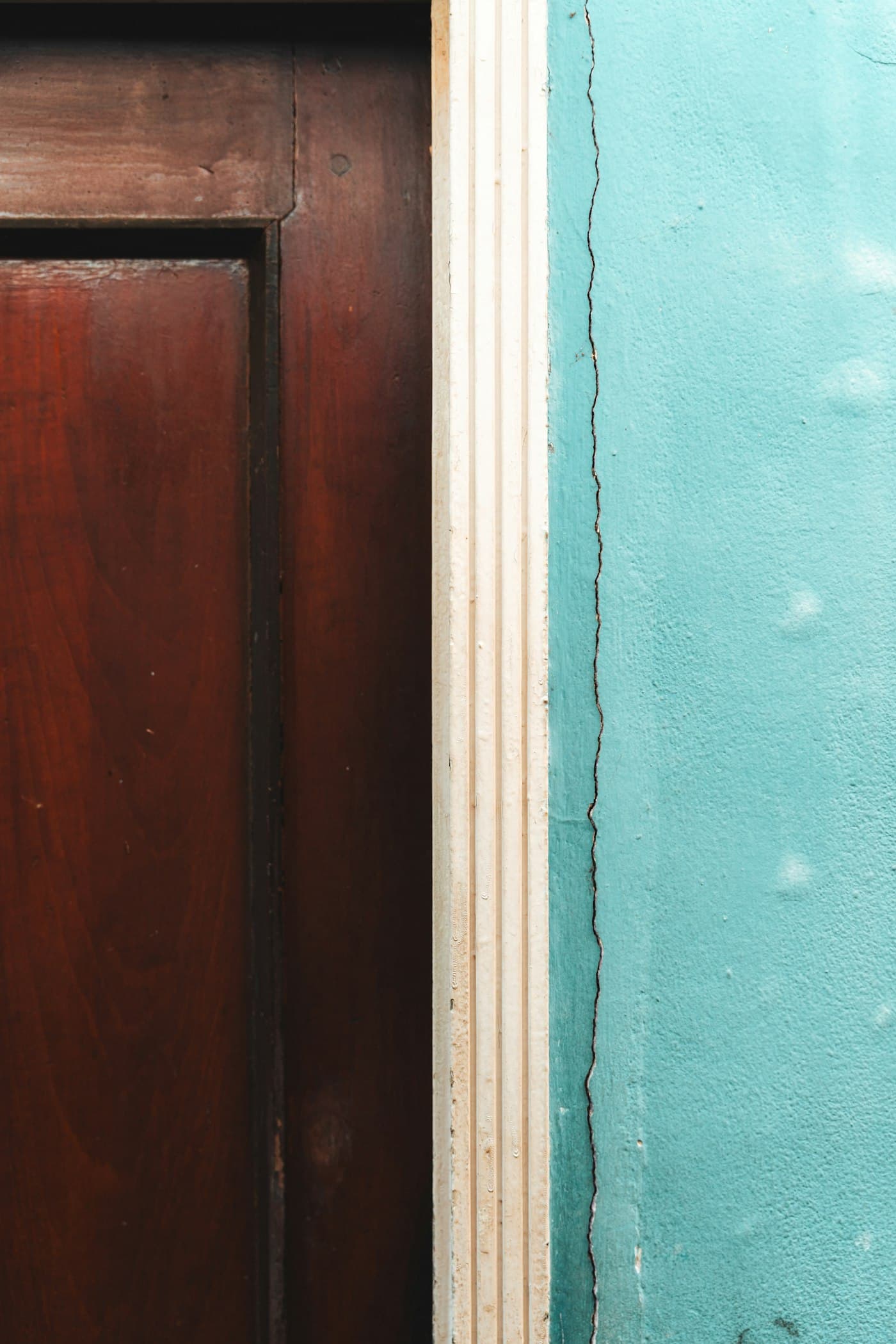 Close-up detail where a dark wood door meets a painted teal wall and trim