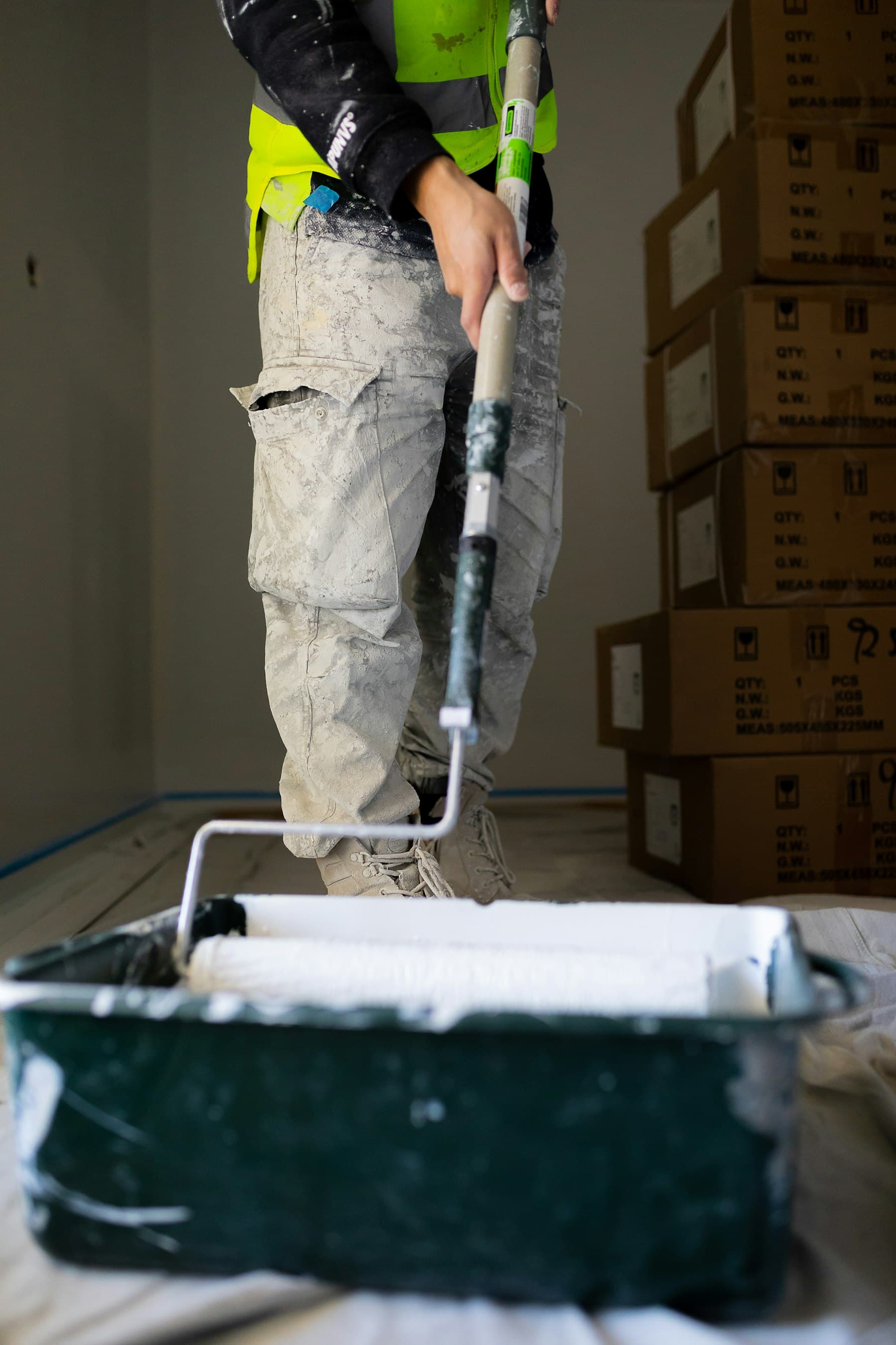 A painter in workwear rolling white paint onto an interior wall