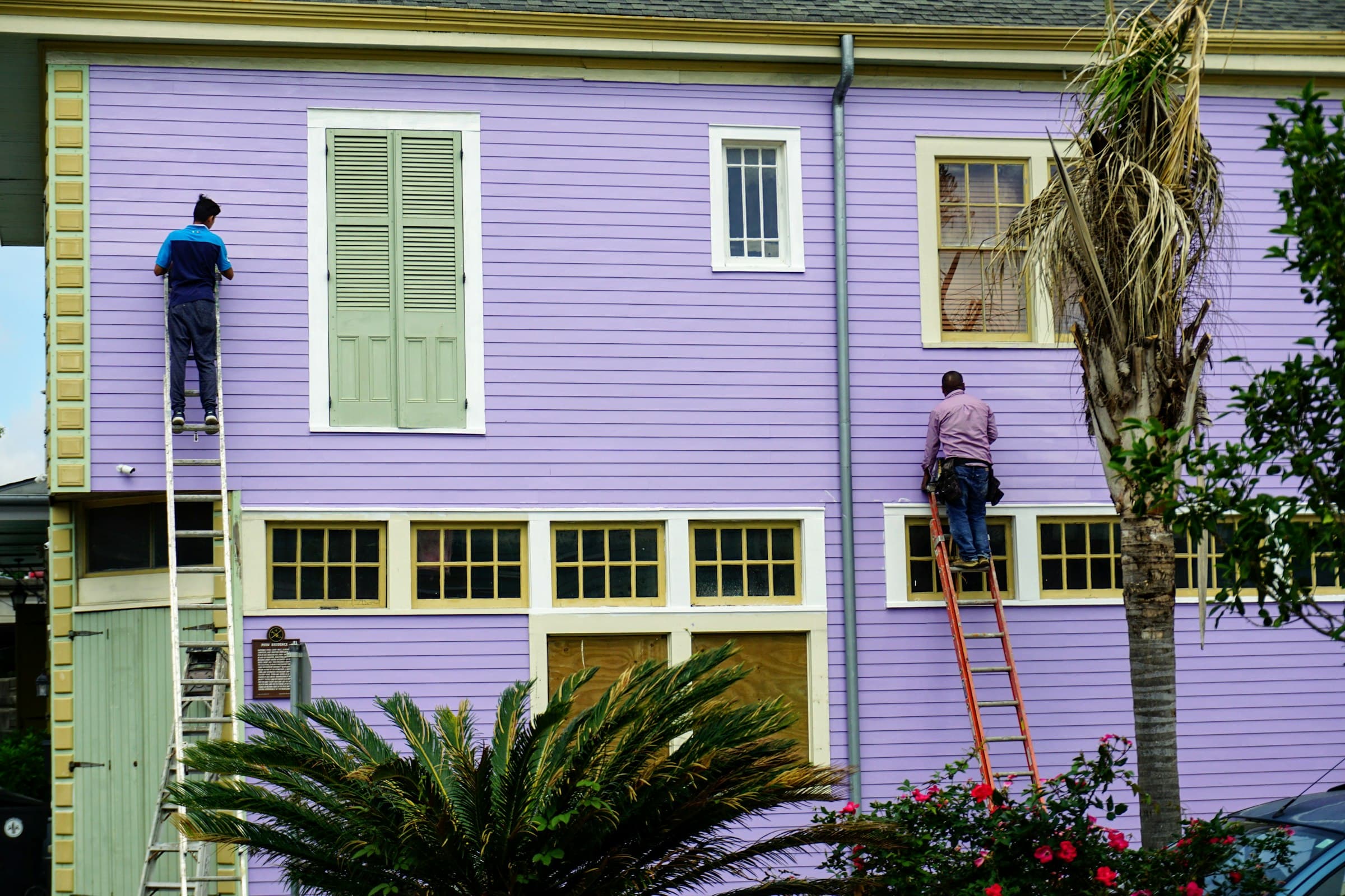 Two painters actively painting the wood siding of a colorful American house