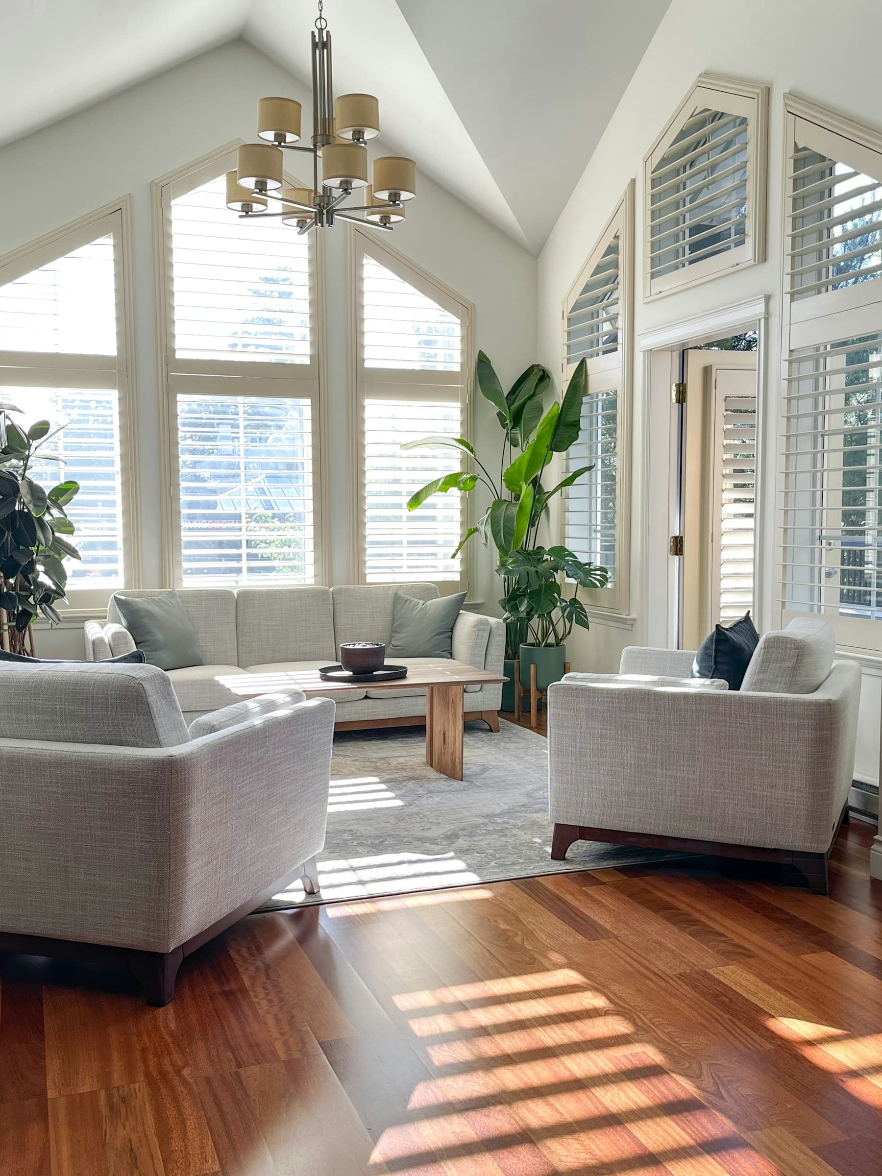 A bright, freshly painted living room with vaulted ceilings and plantation shutters