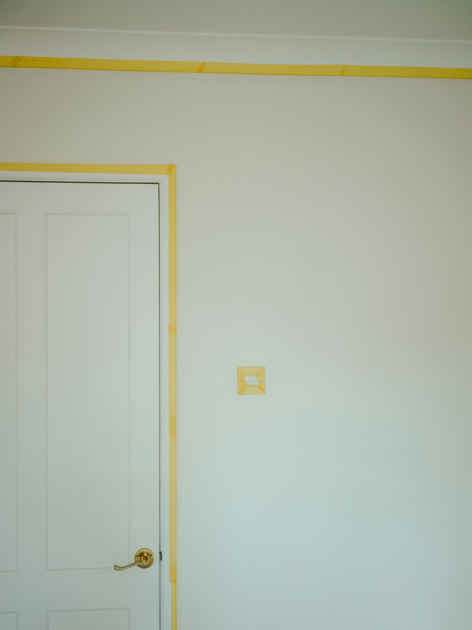 Yellow painter's tape cleanly masking a white door frame before trim painting